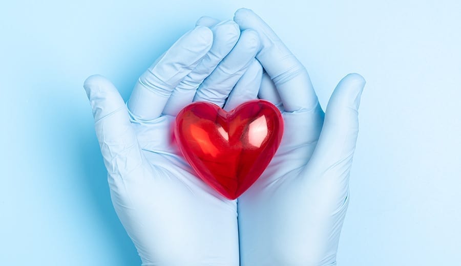 Händer med läkarhandskar som håller i ett rött hjärta gjort i glas