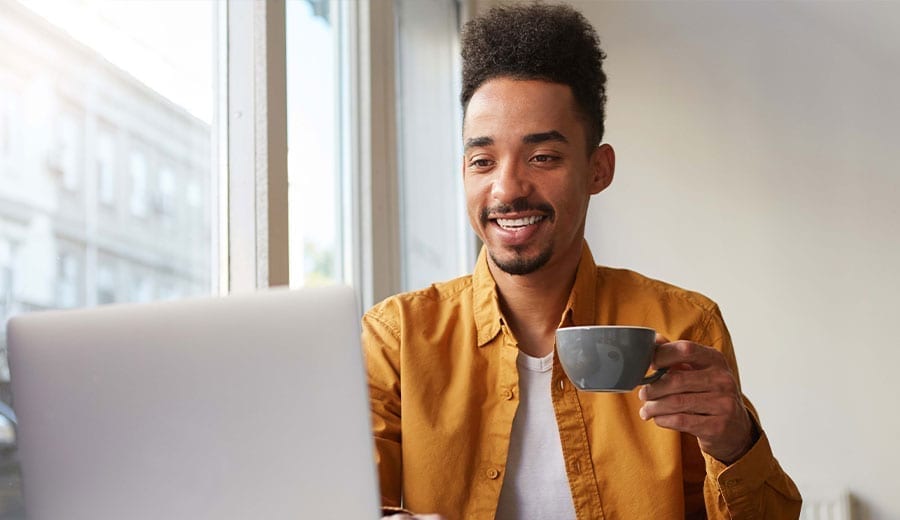 En man som dricker kaffe framför en dator